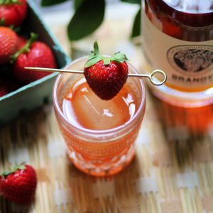 strawberry old fashioned served on a large ice cube with a strawberry garnish