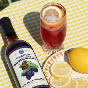 bottle of Brambleberry Bourbon next to lemon slices and a glass of Brambleberry lemonade